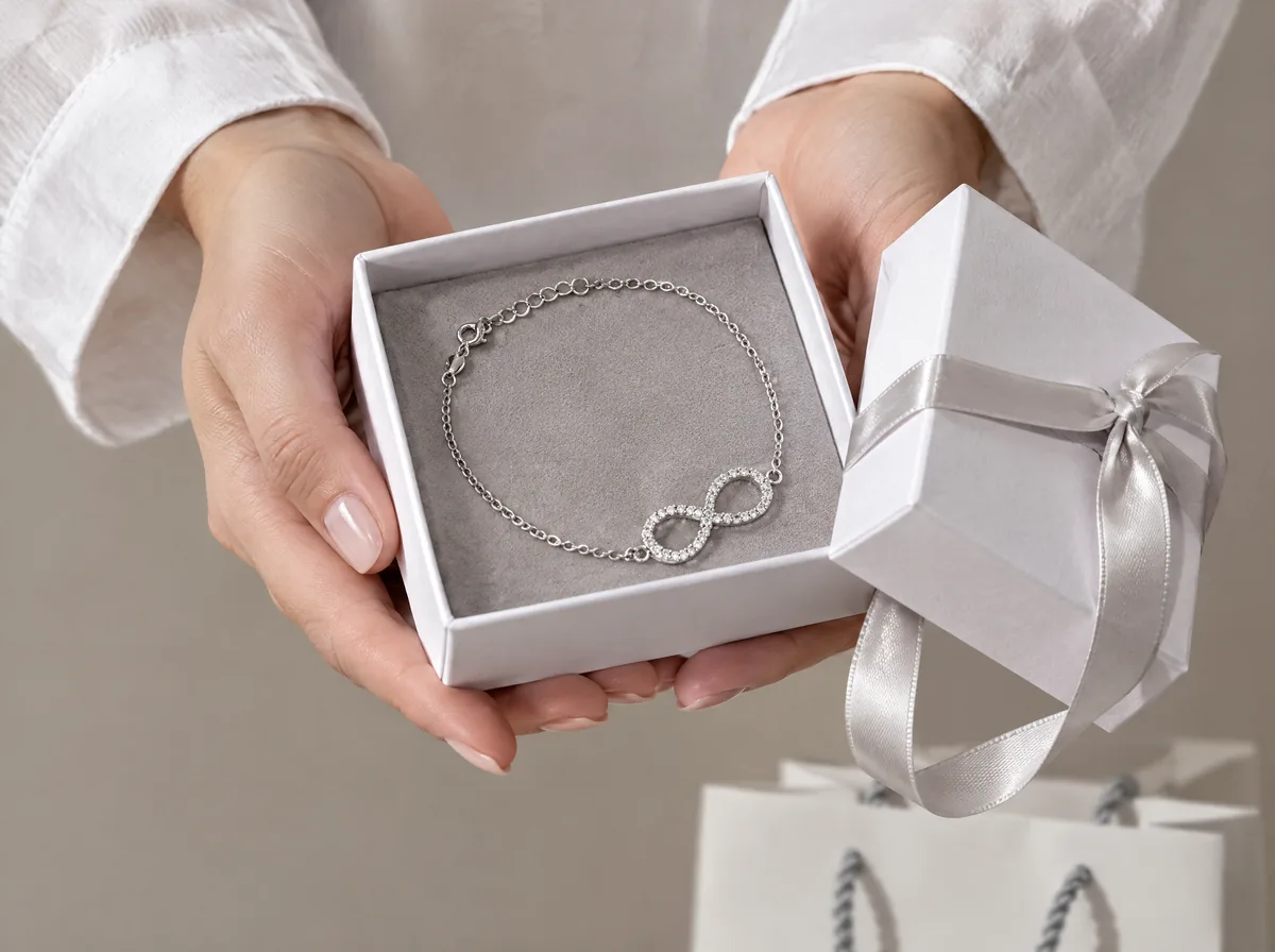 Mani di donna che offrono una confezione regalo Malì aperta con un bracciale infinito in argento